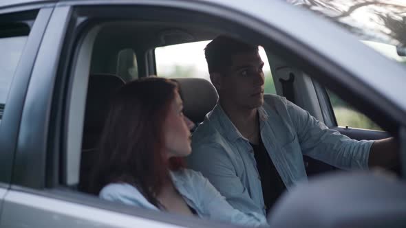 Young Positive Couple Sitting in Car Discussing Trip Route alt