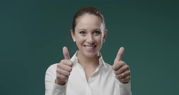 Happy young woman in white shirt giving a thumbs up and smiling at camera