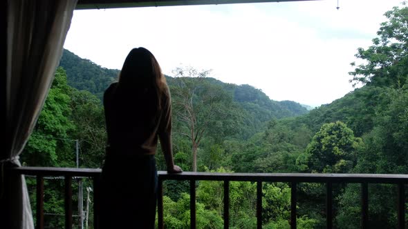 Rear view of a woman standing on balcony and looking at a beautiful mountains and nature view