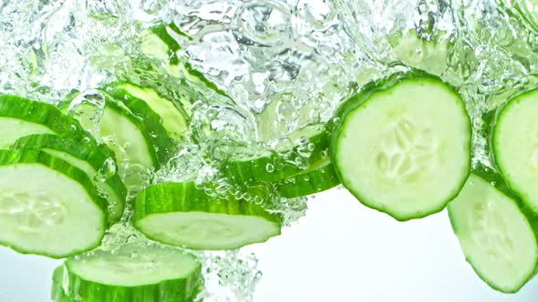 Super Slow Motion Shot of Cucumber Slices Falling Into Water on White Background at 1000Fps. alt