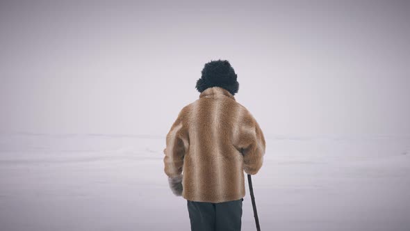 Indigenous Old Man with Stick Walking Away on Frozen Ice Outdoors alt