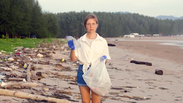 Woman with Trash Bag Clears Beach From Plastic Bottle in Trash Bag alt