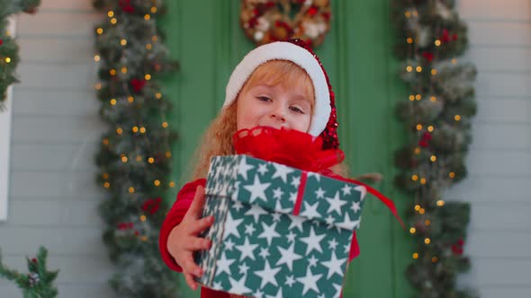 Happy Toddler Child Girl Kid in Red Sweater Gifting One Christmas Present Box Stretches Out Hands alt