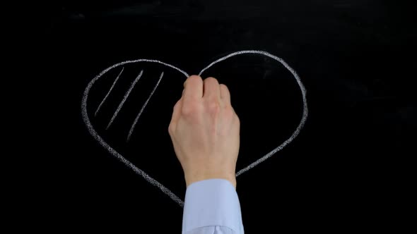 Male hand draws heart symbol in chalk on a blackboard. Close up. HD