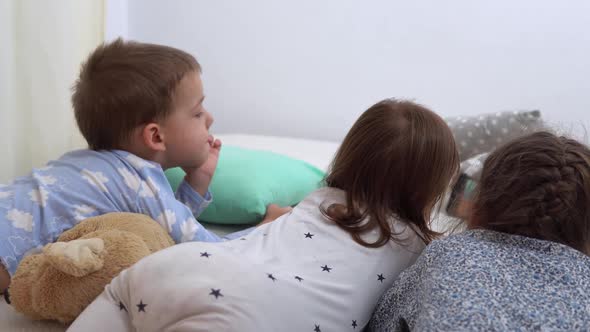 Smiling Preschool Toddler Children In Pajamas Watching Cartoon on Smartphone on Bed