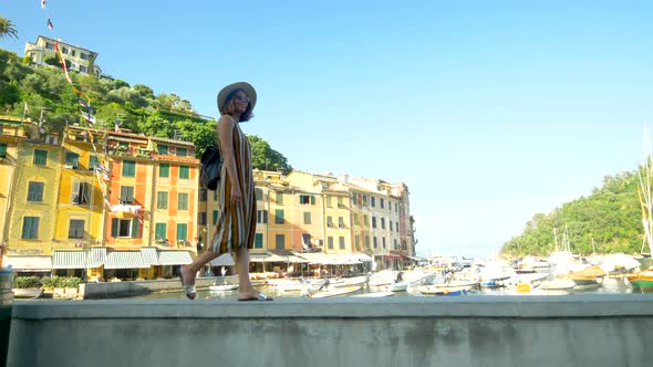 A woman walking wearing hat and backpack purse traveling, Portofino, Italy, luxury resort, Europe alt