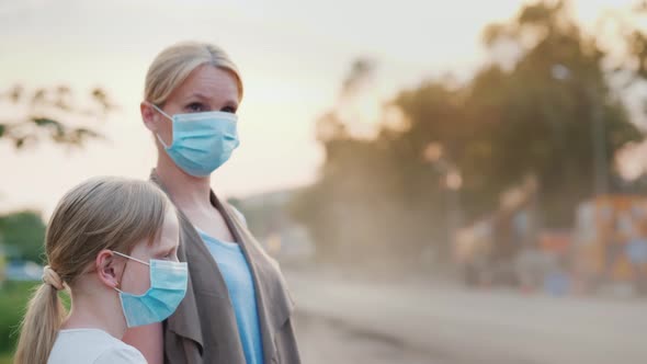 Family in Protective Masks are Standing Near a Dirty Dusty Road in the City alt