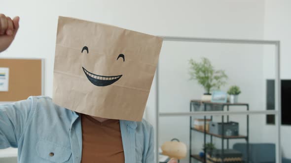 Slow Motion Portrait of Cheerful Employee Wearing Breadbag with Emoji on Head Dancing in Office alt