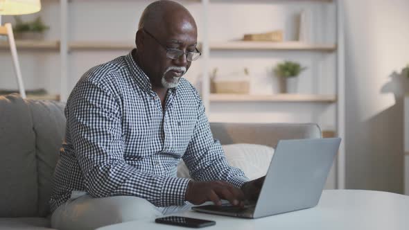 Serious Elderly African American Man Freelancer in Eyeglasses Typing on Laptop Working From Home alt