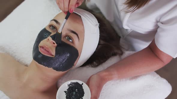 Caucasian woman lying back while beautician gives her a face mask alt