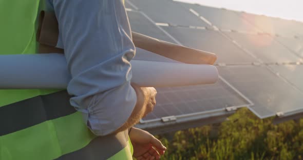 Crop View of Male Person Carrying Scrolls of Engineering Drawing While Walking Near Photovoltaic alt