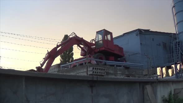 A Red Excavator Stands on a Platform Near the Plant. Storage Earthmoving Machine Behind Barbed Wire alt