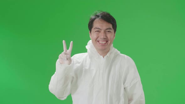 Male Wear Protective Uniform PPE Take Off Mask And Smiling With Victory Hand Sign In Green Screen alt