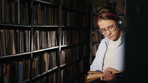 A Teenager in a Library Reads a Book in the Evening