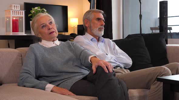 An Elderly Couple Sits on A Couch in An Apartment, the Man and Woman Sulk and Ignore Each Other alt