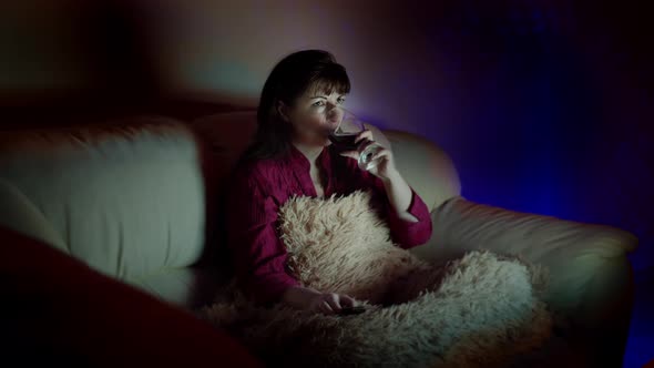 Brunette Woman Relax at Home with a Glass of Wine on the Sofa and Watches Tv in the Evening