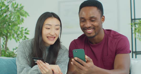 Attractive Young Mixed Ethnicity Couple with Smartphone and Credit Card Shopping on the Internet alt