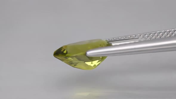 Natural Peridot Gemstone in the Tweezer on the Background
