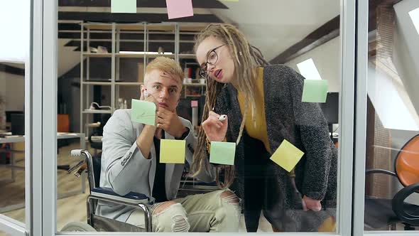Man in Wheelchair and Girl Talking with Each other While Analyzing Details of Joint Project alt