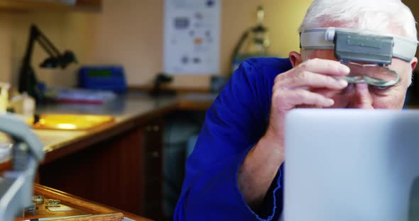 Horologist using laptop while repairing a watch alt