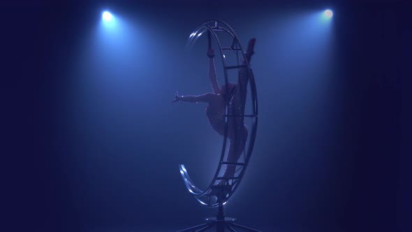 Gymnast Rotates on a Metal Structure Moon in a Vertical String. Blue Smoke Background alt