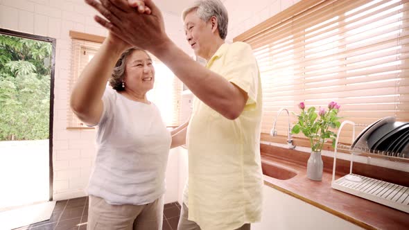 Asian elderly couple dancing together while listen to music in kitchen at home.