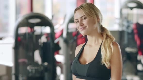 Fitness Woman Showing Thumb Up and Winking Eyes on Sport Club Background alt