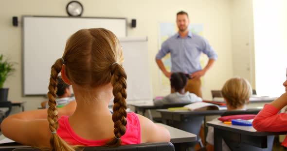 Multi-ethnic schoolkids raising hands while sitting at desk in a classroom at school 4k alt
