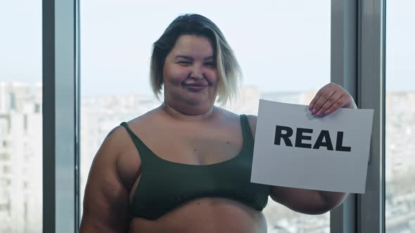 An Overweight Woman Holding a Nameplate with a Sign PERFECT and Replaces It with a Sign REAL Holding alt