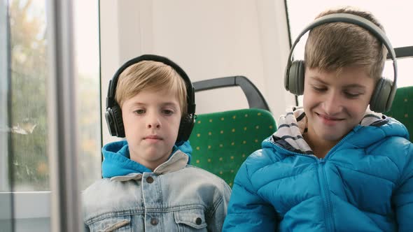 Two Boys In The Passenger Seat On The Bus Playing Smartphones alt