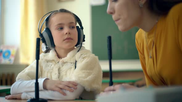 Young Girl and Teacher Using Headphones and Microphone in the Classroom alt