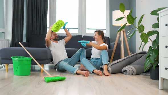 Tired Couple Sits on the Floor in a Room and High Five Each Other After They Finish Cleaning the alt