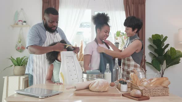 Happy moment. African American parents tie apron on kids before making bread dough