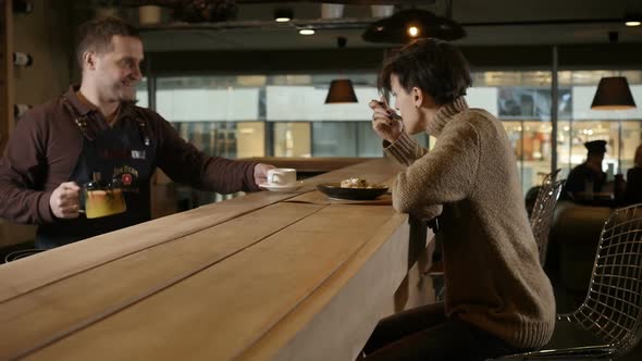 a Girl Eats Merrily Sitting in a Restaurant and Talks to the Waiter alt