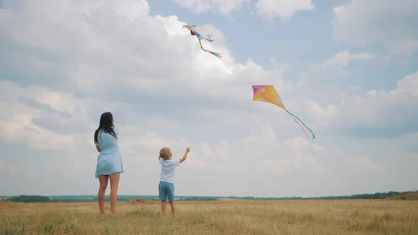 Happy Family Mom and Son Playing with Flying Kite on Meadow in Beautiful Sunny Day Blue Sky alt
