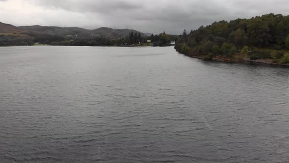 Tilting down over dark Loch Ness water on cloudy day, aerial alt