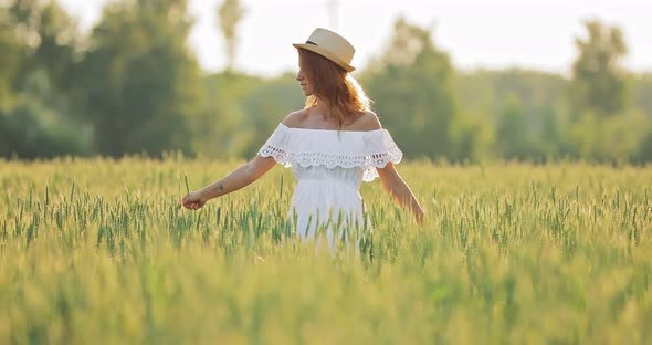 Pretty Girl with an Ear of Wheat Walks Through a Green Field in Summer and Enjoys Nature alt