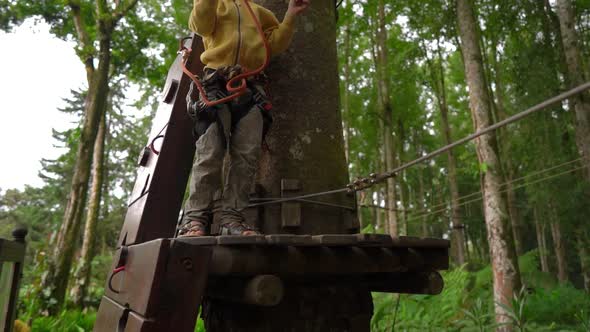 Superslowmotion Shot of a Little Boy in a Safety Harness Climbs on a Route in Treetops in a Forest alt