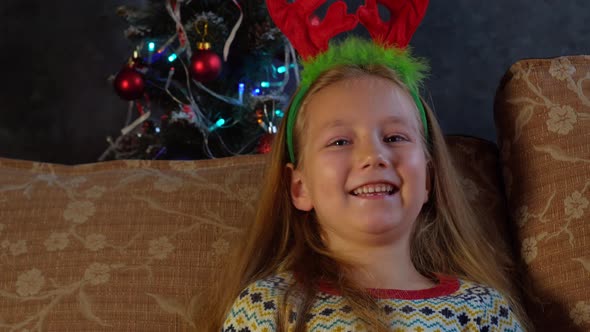 Happy little girl in red deer horns laughs and looks into camera at home 4K face portrait Smiling alt