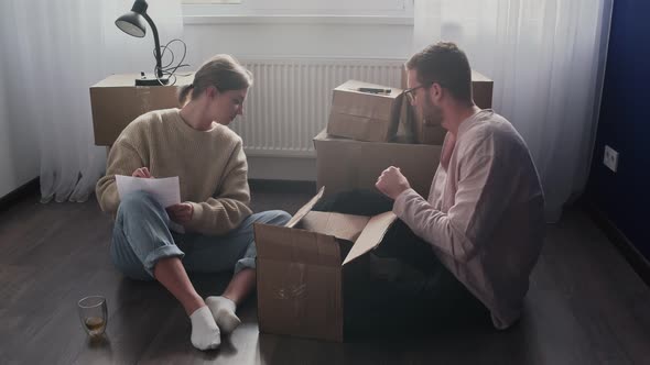 Happy Couple Packing Cardboard Boxes Prepare to Moving Out Relocation Family Sitting on Floor in alt