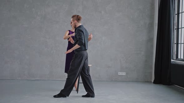 Man Showing Woman Tango Elements in Grey Studio Against Large Windows