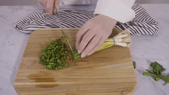 Step by step. Chopping organic green onions on a wood cutting board. alt
