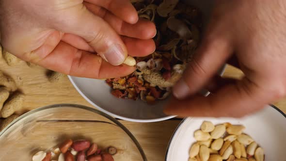 Slow motion footage of men's fingers peeling peanuts stacking them in a bowl. Close-up alt