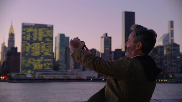 Man in New York City taking photos of city with cell phone