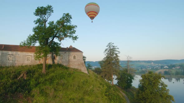 Colorful Hot Air Balloons Fly Over the Medieval Castle and Lake in the Morning Fog. Maneuverable alt