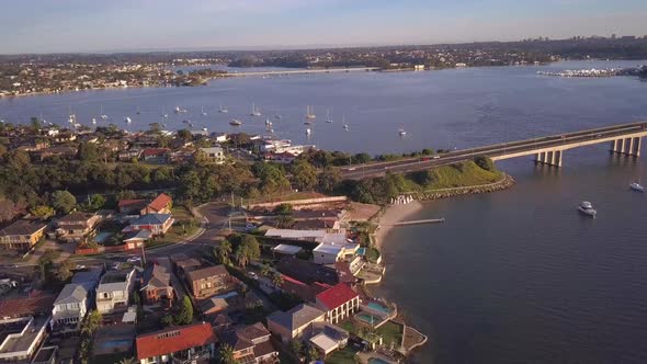Aerial view of waterfront houses with ocean view and many boats and a long bridge. Drone panning rig alt
