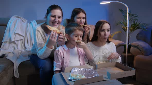 Happy Family Smiling and Laughing While Eating Pizza and Watching TV Movie or Show at Night alt