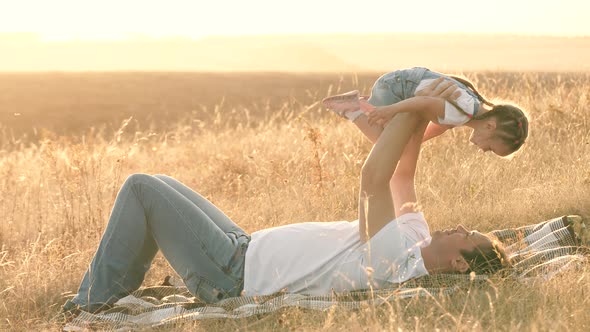 Dad Plays with His Little Daughter in the Park on a Blanket. Child Flies in the Arms of Dad, the Kid alt