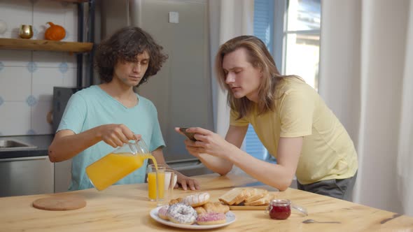 Happy Young Men Using Mobile Phone While Having Breakfast at Home alt