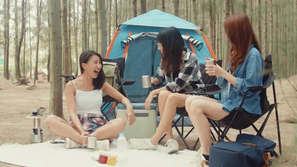 Group of young asia camper friends sitting in chairs by tent in forest.